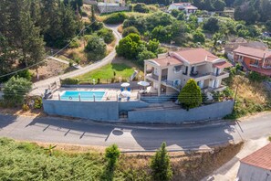 A two-story house with a swimming pool, surrounded by greenery and a road.