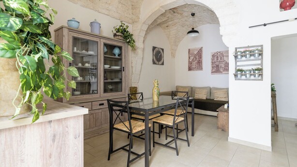 A dining area with a glass table and chairs, a wooden cabinet with glass doors, and a plant on the counter. - Terrazza 42 by Wonderful Italy (Ostuni)