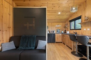 Un interior moderno con un sofá oscuro, paredes de madera, una zona de cocina y un taburete de bar.