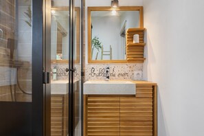 Un bagno con cabina doccia in vetro, mobile bagno in legno con lavabo e specchio sopra il mobile.