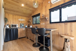 Un interior de madera con una zona de cocina, taburetes de bar y una ventana con vistas.