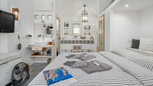 A bedroom with a bed, a dresser, a mirror, a sink, and a television.