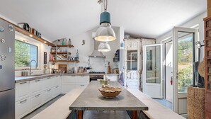 A modern kitchen with a central island, pendant lighting, and a view through an open door.
