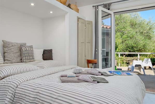 A bedroom with a large bed, a sliding glass door to a balcony, and a view of greenery outside.