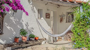 A white building with terracotta roof tiles, a hammock, and potted plants.