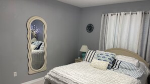 Ein Schlafzimmer mit Bett, Spiegel, Uhr und Vorhängen.