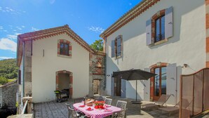 A courtyard with a table set for dining, outdoor chairs, and a sun umbrella. - Cozy home in Privas with sauna (Privas)