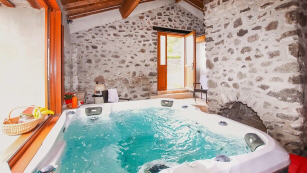 A stone-walled room with a hot tub, wooden beams, and a door leading outside. - Cozy home in Privas with sauna (Privas)