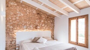 A bedroom with a stone wall, a bed with pillows, a wooden headboard, and a window. - Finca 'Son Sec Nou' with Mountain Views, Wi-Fi and Air Conditioning (El Palmer)