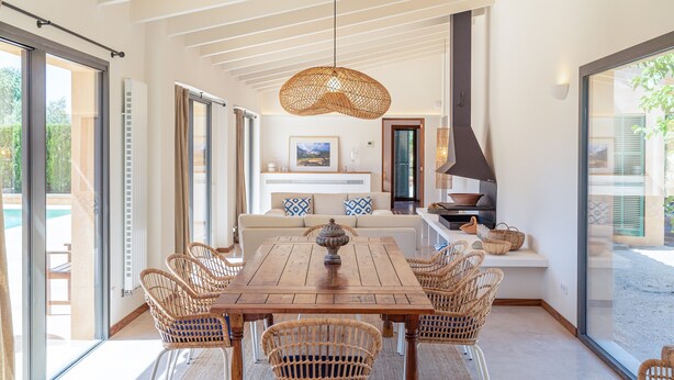 A dining area with a wooden table, wicker chairs, a hanging light fixture, a sofa with patterned cushions, and a view of the outdoors. - Holiday Home 'S'hort Des Frares' with Mountain View, Wi-Fi and Air Conditioning (El Palmer)