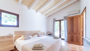 A bedroom with a bed, wooden headboard, bedside tables, a window, and an air conditioning unit. - Holiday Home 'S'hort Des Frares' with Mountain View, Wi-Fi and Air Conditioning (El Palmer)