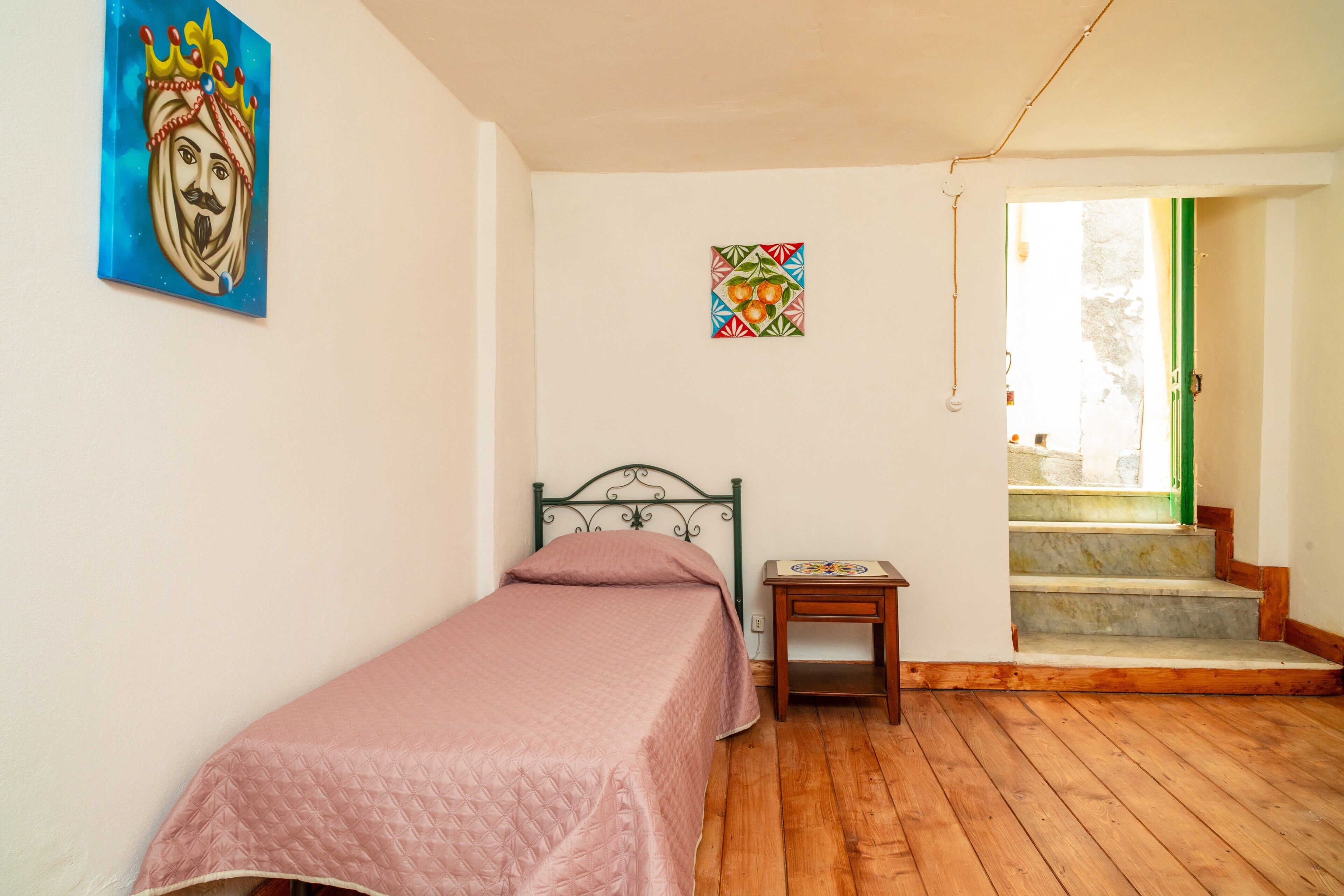 Een slaapkamer met een bed, een tafeltje, een schilderij en een trap naar een buitenruimte.