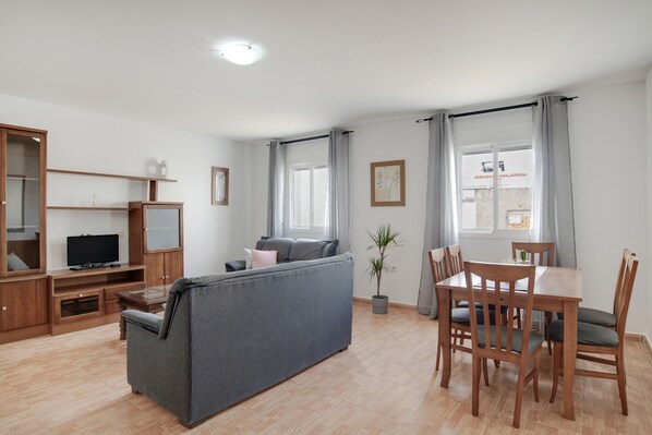 Un salon comprenant un canapé, un téléviseur, un meuble de rangement en bois, une table à manger avec des chaises et une plante en pot.