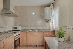 Une cuisine dotée de plans de travail en granit, de meubles en bois, d’un four à micro-ondes, d’une cuisinière et d’un chauffe-eau.