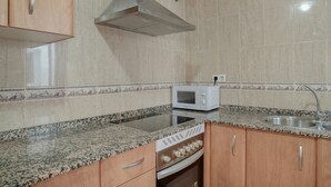 Een keuken met granieten aanrechtbladen, een inbouwmagnetron, een roestvrijstalen spoelbak en houten kastjes.