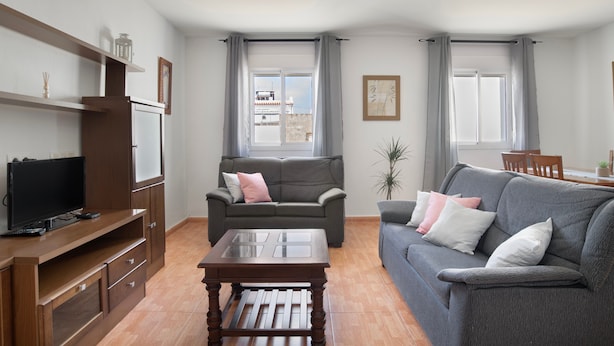 Een woonkamer met een bank, een salontafel, een tv op een houten standaard, en een eethoek met stoelen en een tafel.