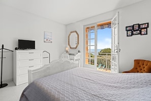 A bedroom with a bed, a dresser, a television, a mirror, and a balcony with a view.