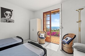 A bedroom with a bed, a wardrobe, a wicker chair, a bedside table, and a view of the outside.