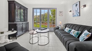 A modern living room with a dark sofa, two small tables, a white console table, and a large window with a view of greenery. - Holiday Home 'La Belle Provence' with Sea View, Wi-Fi and Air Conditioning (Roquebrune-sur-Argens)