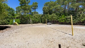 Una cancha de voleibol de arena, con una red, rodeada de árboles.