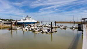 Un puerto deportivo con varias embarcaciones amarradas, un barco grande al fondo y un cielo despejado.