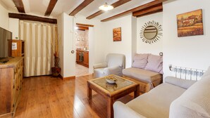 A living room with wooden flooring, a sofa, a coffee table, a chair, and a kitchen in the background.