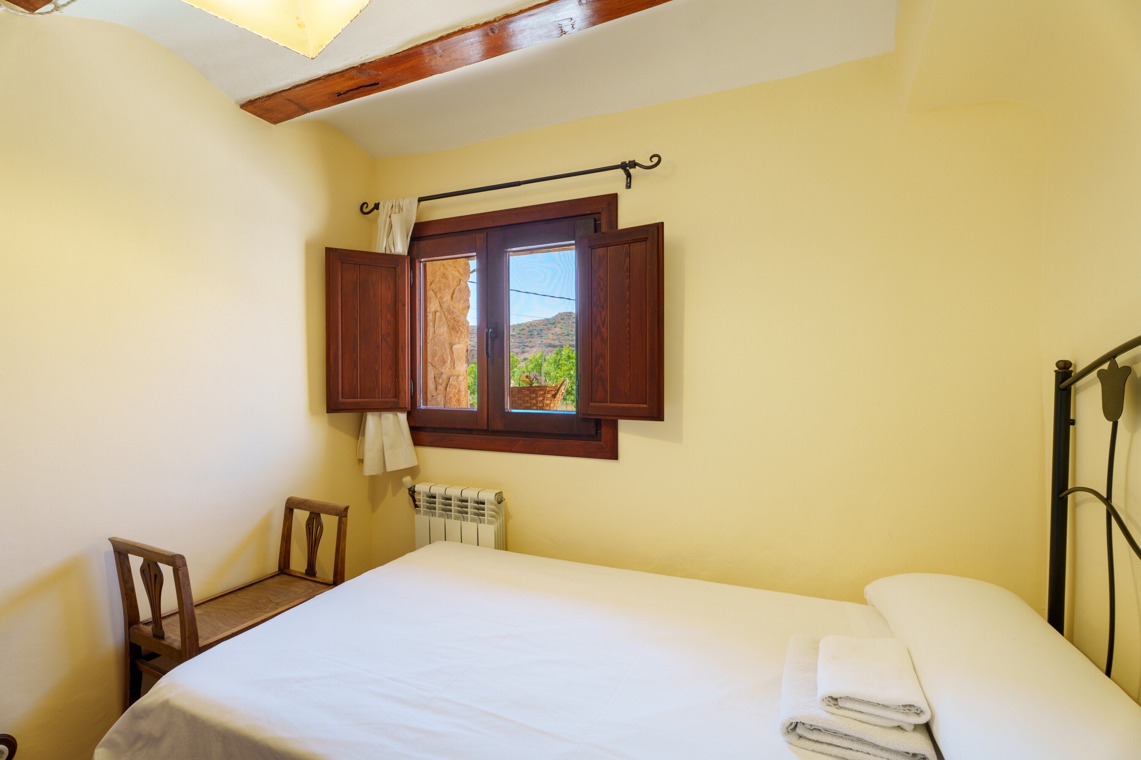 Une chambre avec un lit, une fenêtre avec des volets en bois, un radiateur et une chaise.