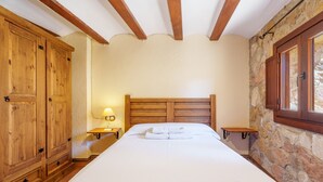 A bedroom with a wooden bed, a nightstand, a wardrobe, and a stone wall.