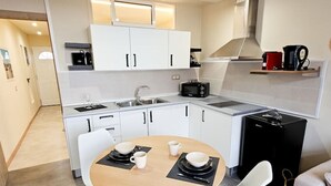 Eine kompakte Küche mit weißen Schränken, einem runden Esstisch mit vier Stühlen, einer Kaffeemaschine und einem Toaster.
