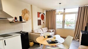 Ein modernes Wohnzimmer mit einer Couch, einem Esstisch und einer Küchenzeile inklusive Schränken und Herd.