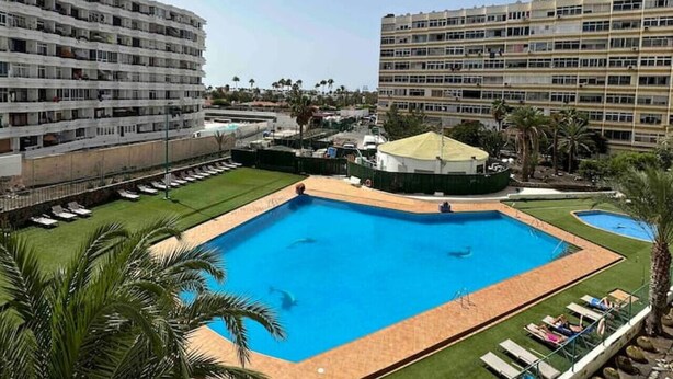 Ein Hotel mit großem, zentral gelegenen Pool, umgeben von Liegestühlen und Palmen.