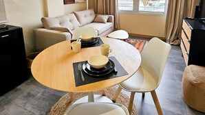 Ein modernes Wohnzimmer mit einer Couch, einem Esstisch für zwei Personen und einem Fernseher.