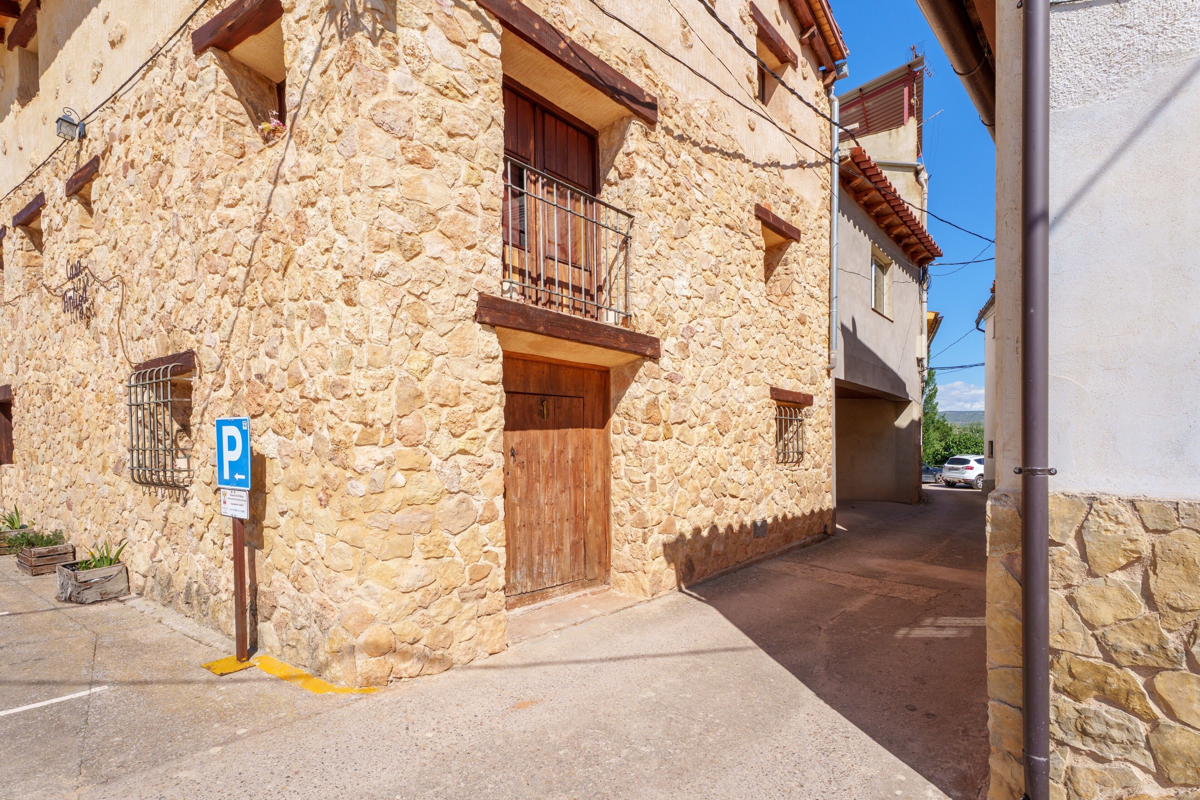 Un bâtiment en pierre avec une porte en bois, un balcon doté d’une rambarde en métal et un panneau indiquant un espace de stationnement.