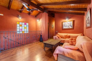 Habitació amb sostre de fusta, un sofà, una taula de cafè, una barana i una paret amb un quadre.