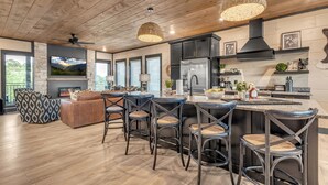 A modern kitchen with a central island, bar stools, and a dining area with a sofa and chairs. - Special Offer•6BD•Pool•Theater•Games•Views (Sevierville)