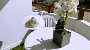 Une chaise blanche et un chapeau blanc sont posés sur une table blanche, à côté d’une orchidée en pot.