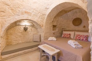 Une pièce aux murs de pierre, avec un lit, un banc et une petite table.