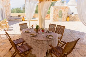 An outdoor dining area with a round table, wooden chairs, and a white tablecloth. - Holiday Home 'Trullo Amami With Private Pool' with Private Pool, Wi-Fi and Air Conditioning (san michele salentino)