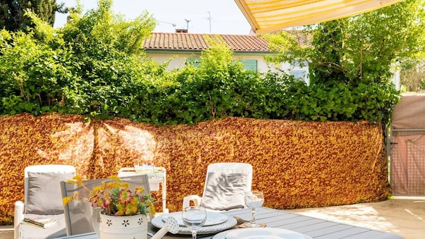 Un espace de restauration en plein air avec une table dressée pour quatre personnes, entourée de chaises, sous une marquise à rayures.