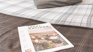 Un lit bien fait, recouvert d’une couverture à carreaux, avec un magazine posé dessus.