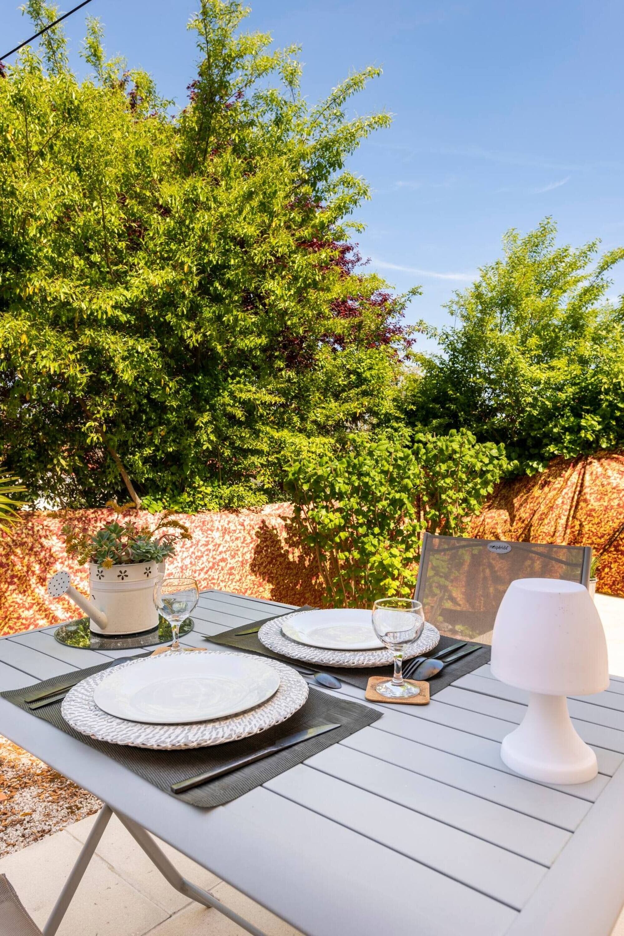 Un área de comedor al aire libre con una mesa lista para dos personas, una planta en maceta y una lámpara.