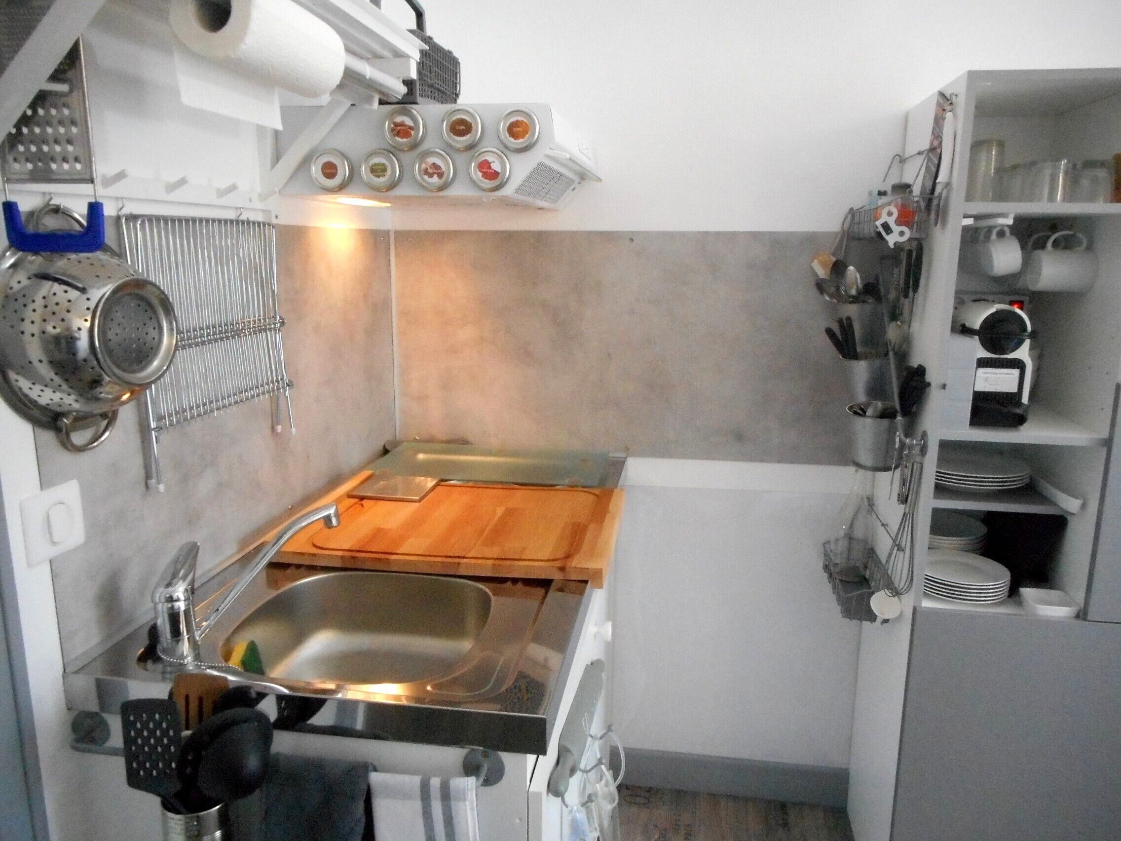 A compact kitchen with a stainless steel sink, a wooden countertop, and a variety of utensils and appliances.