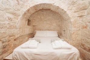 Une chambre aux murs de pierre, avec un lit simple, du linge de lit blanc et des serviettes.