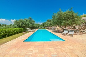 A rectangular swimming pool with a tiled deck, surrounded by lounge chairs and trees.