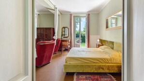 Un dormitorio con cama, una silla, un escritorio, un espejo y vistas al exterior.