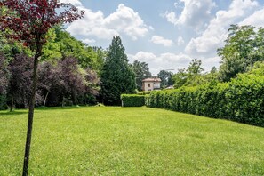 Zona verde y bien cuidada con diversos árboles y un edificio al fondo.