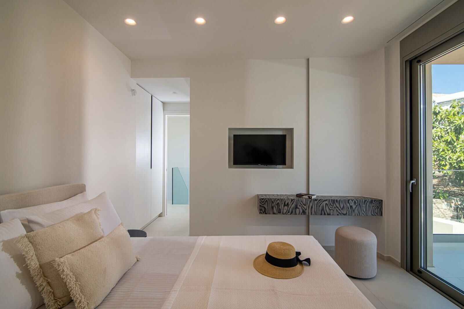 Um quarto moderno com uma cama grande, uma televisão fixada na parede e vista para o exterior através de uma porta deslizante.