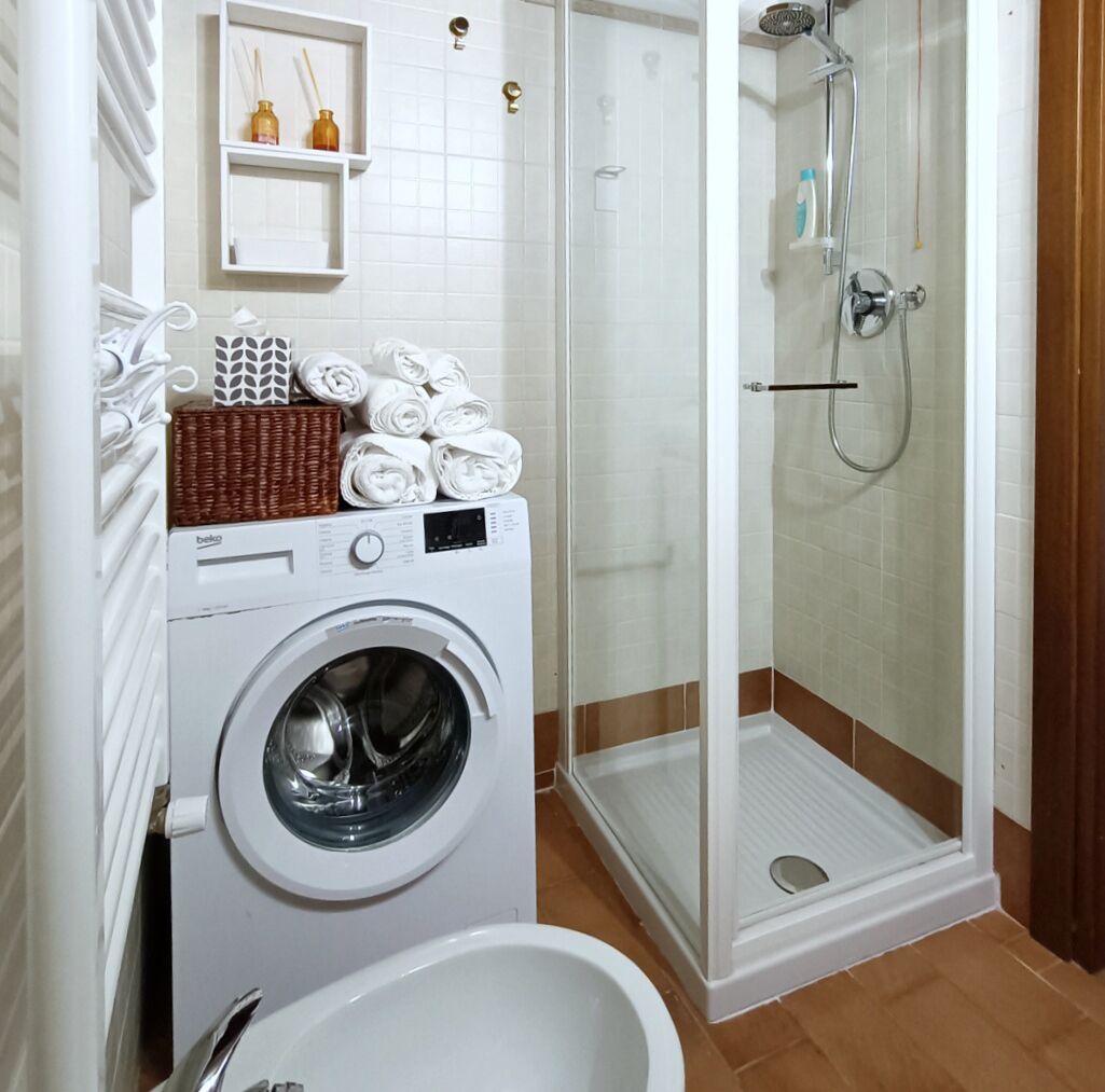 Een kleine badkamer met een wasmachine, een douchecabine en een toilet.