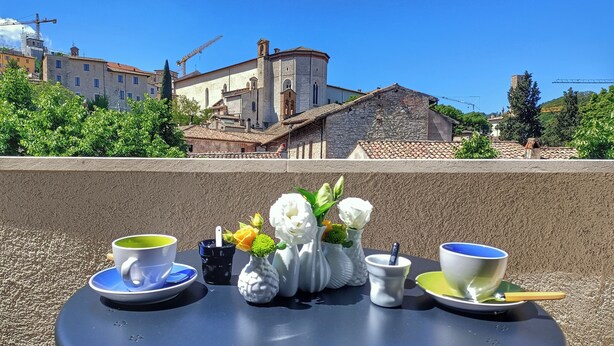 A table with two cups and a vase of flowers on a terrace overlooking a historic building with a tiled roof. - Monastero del Palazzo Casa Vacanze, apartment with panoramic terrace (Spoleto)