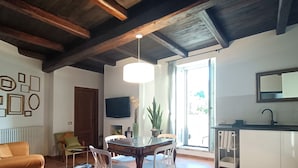 A modern living room with a wooden ceiling, a dining table with chairs, a TV mounted on the wall, and a kitchen area with a sink and cabinets. - Monastero del Palazzo Casa Vacanze, apartment with panoramic terrace (Spoleto)